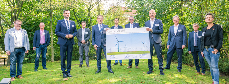 Auf dem Bild halten zwei Männer ein Bild mit Windrädern. Auf dem Bild haben elf Personen unterschrieben, den so genannten Auricher Appell zum Ausbau der Windenergie.