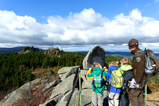 Drei Kinder stehen gemeinsam mit einem Harz-Ranger an der Leistenklippe, Ausblick über den Harz