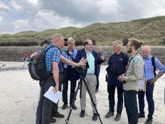 Minister Meyer und Mitarbeiter*innen des NLWKNs auf einem Strandabschnitt auf Spiekeroog, der Minister unterhält sich mit einem NLWKN-Mitarbeiter, vor ihm ist ein Fernglas auf einem Stativ aufgebaut