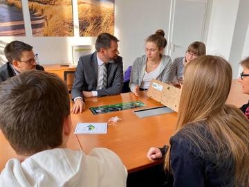 Minister Olaf Lies sitzt mit einer Gruppe von Schülerinnen und Schülern an einem Tisch. Sie spielen ein Brettspiel.