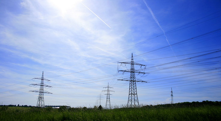Auf dem Foto sind Strommasten vor blauem Himmel zu sehen.