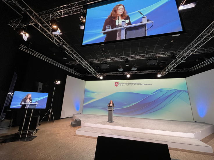 MU-Mitarbeiterin Lena Hübsch spricht an einem Rednerpult. Im Hintergrund ist das Logo des Umweltministeriums zu sehen.