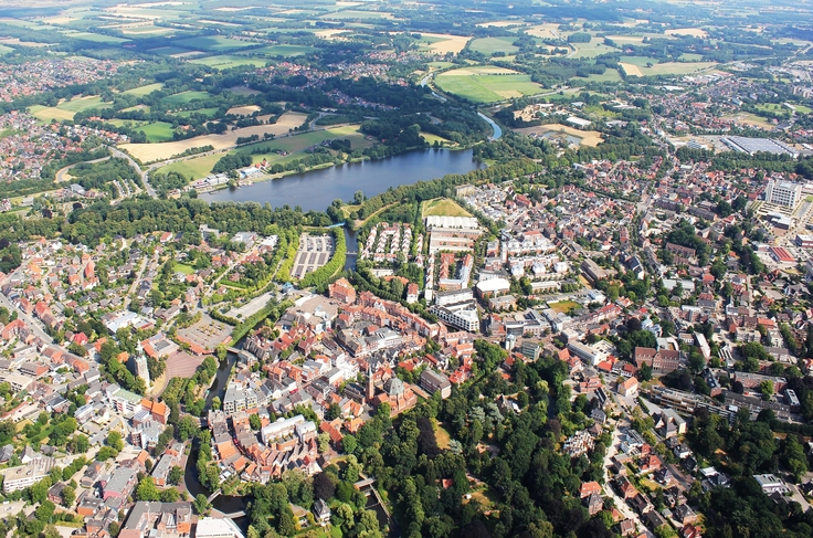Man sieht eine Luftaufnahme von der Stadt Nordhorn: Die Stadt umgibt einen See, an den Häusern fließt ein Fluss vorbei.