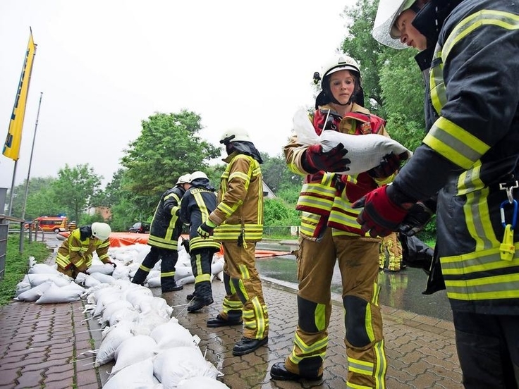 Feuerwehrkräfte reichen sich gegenseitig Sandsäcke an, um einen Wall gegen Hochwasser zu erstellen