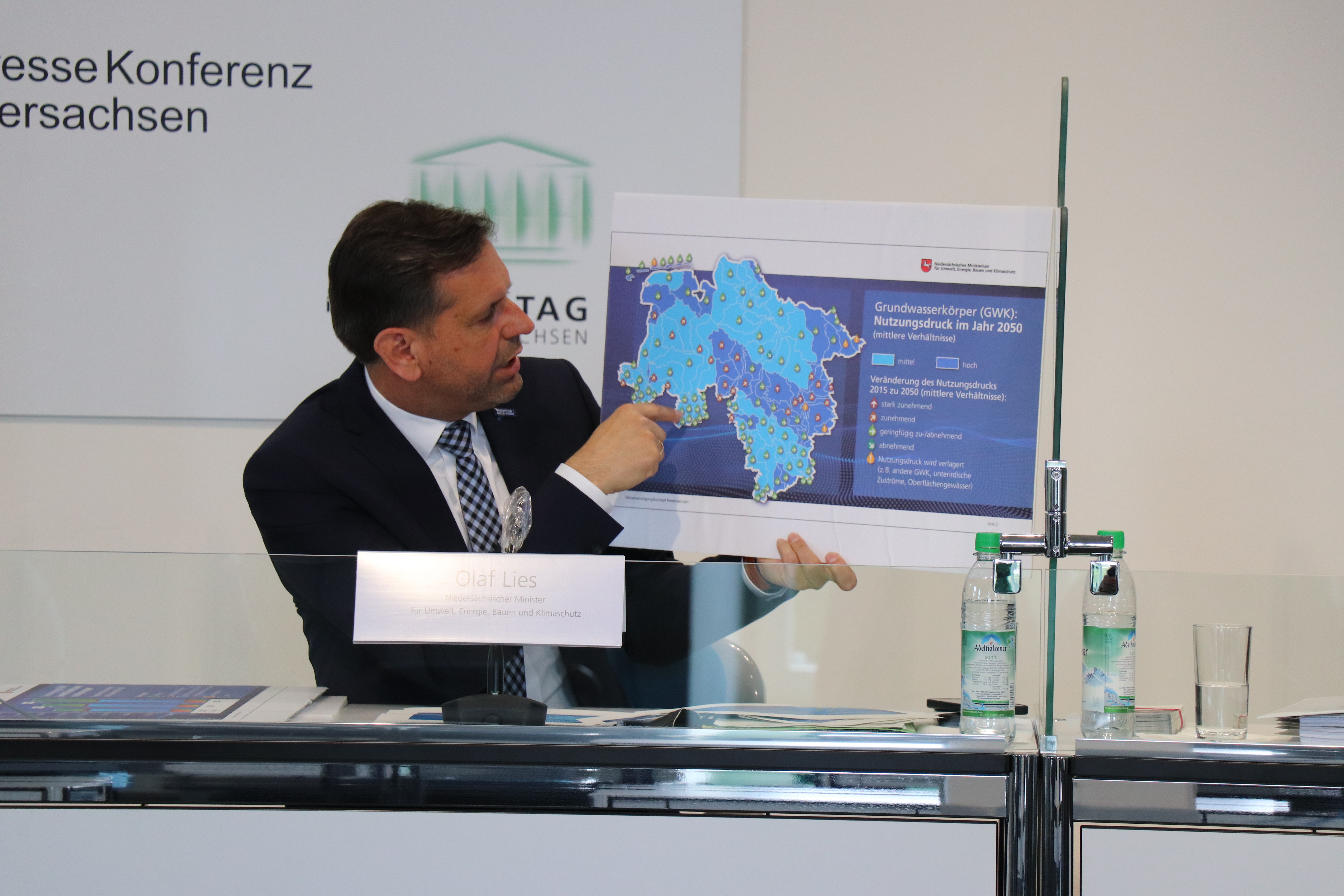 Minister Lies sitzt an einem Podium und deutet auf eine Karte Niedersachsens, um das Wasserversorgungskonzept vorzustellen